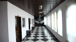 A hotel corridor with a checkered floor, ceiling fans, and large windows. - Hotel L S Restaurant & Spa (Udaipur)