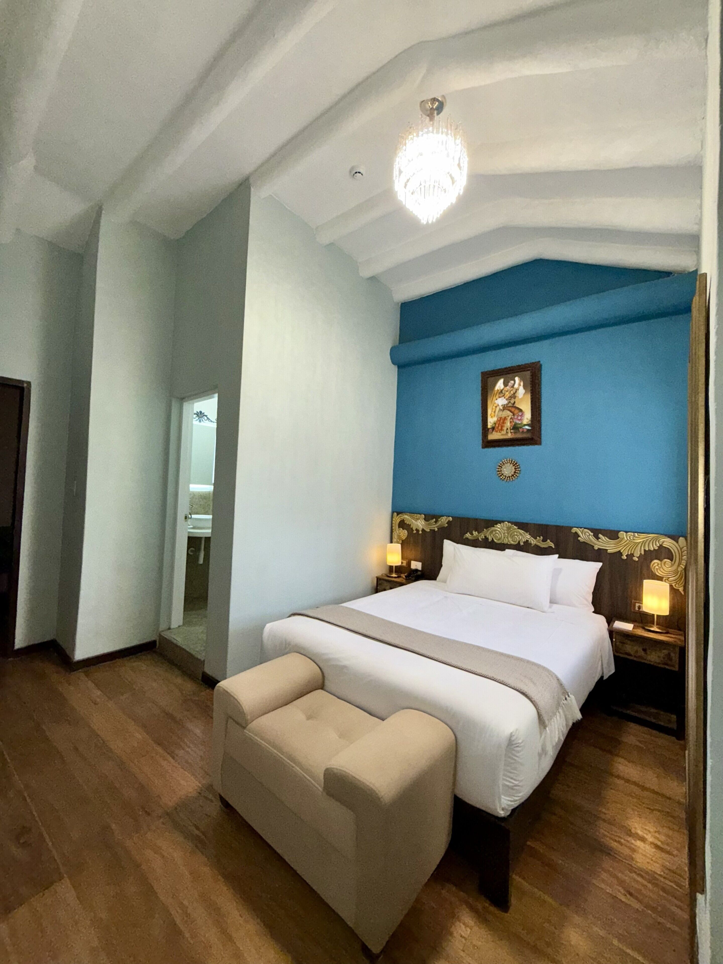 Habitación de hotel con una cama grande, una mesita de noche, un espejo, una araña y una pared de acento azul.