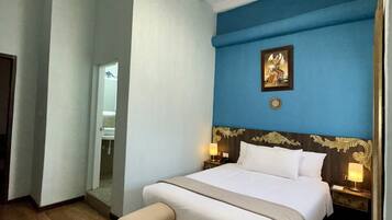 Habitación de hotel con una cama grande, una mesita de noche, un espejo, una araña y una pared de acento azul.