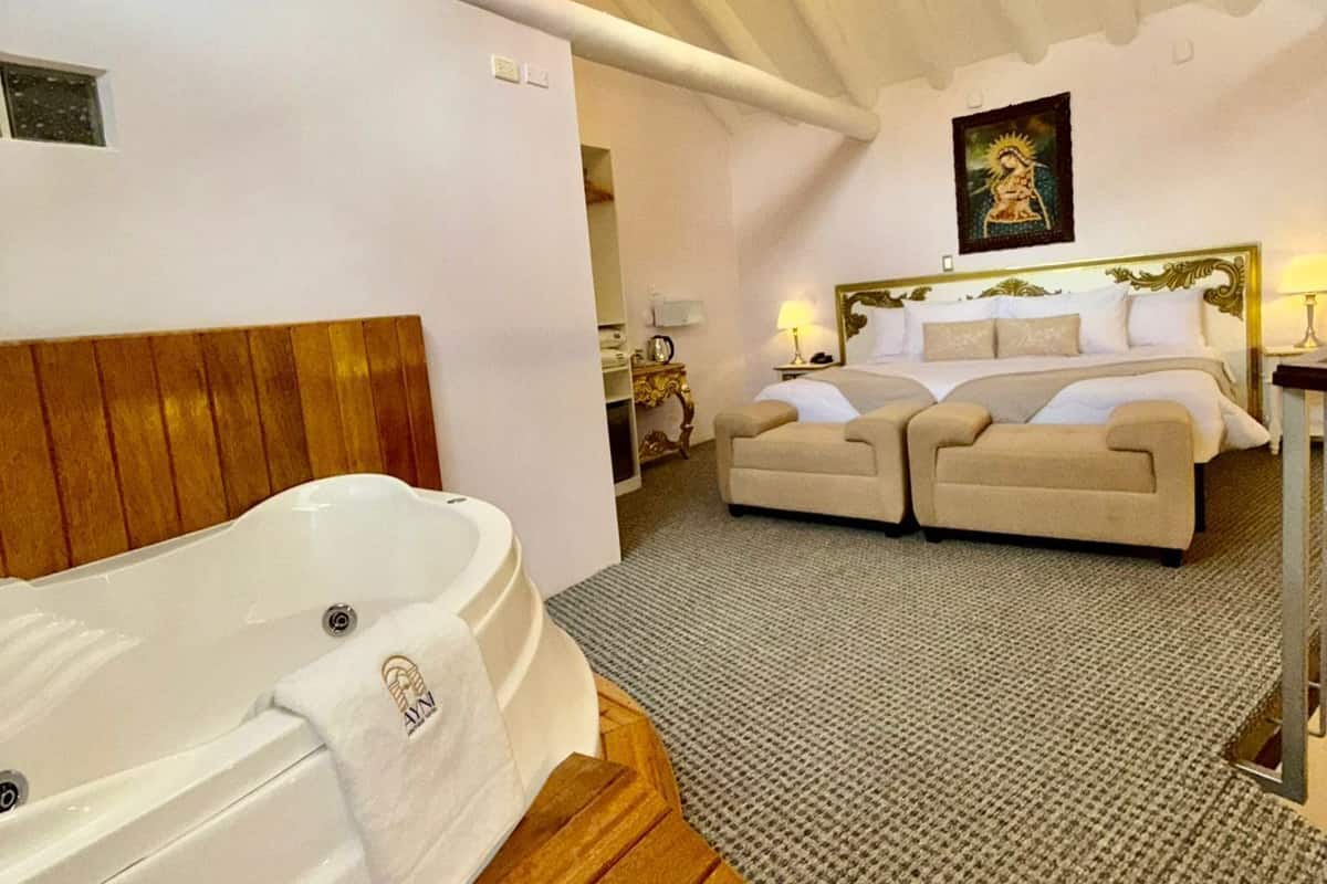 Ein geräumiges Schlafzimmer mit einem großen Bett, einer separaten Sitzecke, einer Badewanne und einem Kronleuchter.