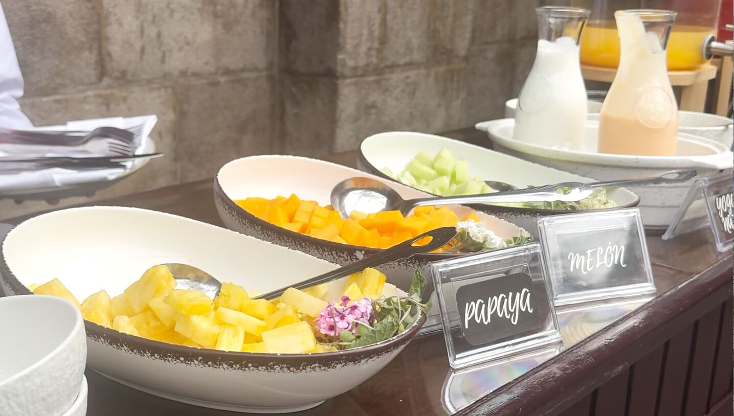 A buffet with labeled bowls of papaya, melon, and other fruits.