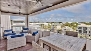 A covered outdoor area with wicker furniture and a wooden table, overlooking a residential area. - Caspian Escape (Santa Rosa Beach)