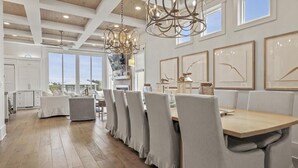 A modern dining area with a long table, cushioned chairs, and pendant lighting. - Caspian Escape (Santa Rosa Beach)