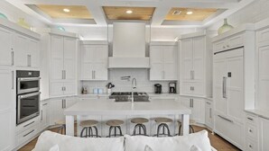 A modern kitchen with white cabinetry, a central island with stools, and built-in appliances. - Caspian Escape (Santa Rosa Beach)