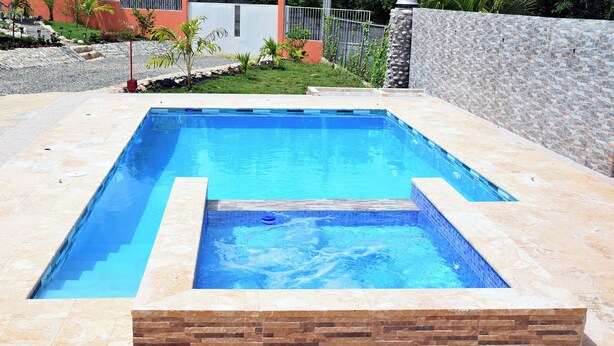 A rectangular swimming pool with clear blue water, surrounded by a stone wall and a tiled deck.