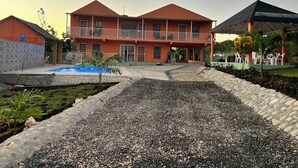 A two-story building with a swimming pool, a covered patio area, and a landscaped garden.