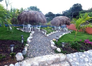 Un espace jardin agrémenté de parasols en chaume, de chaises en plastique blanc et d’un chemin de gravier.