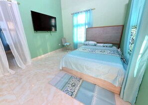 Une chambre à coucher avec un lit, une chaise, une télévision et une fenêtre avec des rideaux.