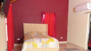 A bedroom with a bed, red curtains, and an air conditioning unit.