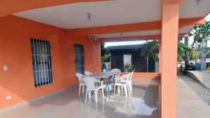 A covered patio area with a tiled floor, a white table with chairs, and a window with metal bars.
