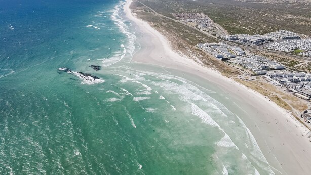 An aerial view of a coastal area with a beach, buildings, and mountains. - 17 Megan's Place - Two Bedroom Apartment, Sleeps 3 (Blouberg)