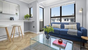 A modern apartment with a kitchen, a living area with a blue sofa, and large windows. - 17 Megan's Place - Two Bedroom Apartment, Sleeps 3 (Blouberg)