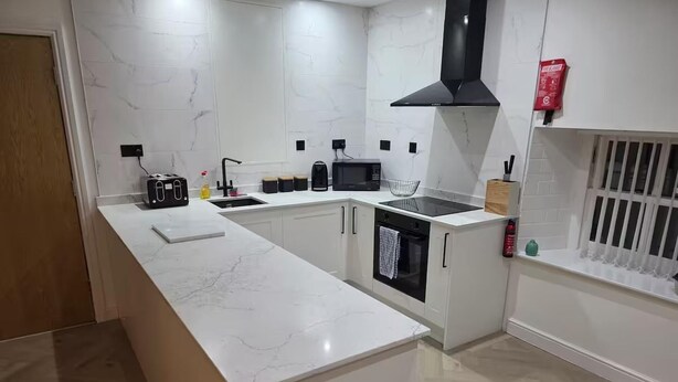 A modern kitchen with white marble countertops, a black range hood, and a built-in oven. - Liverpool Penthouse - Sleeps 8 - City Centre (Liverpool)