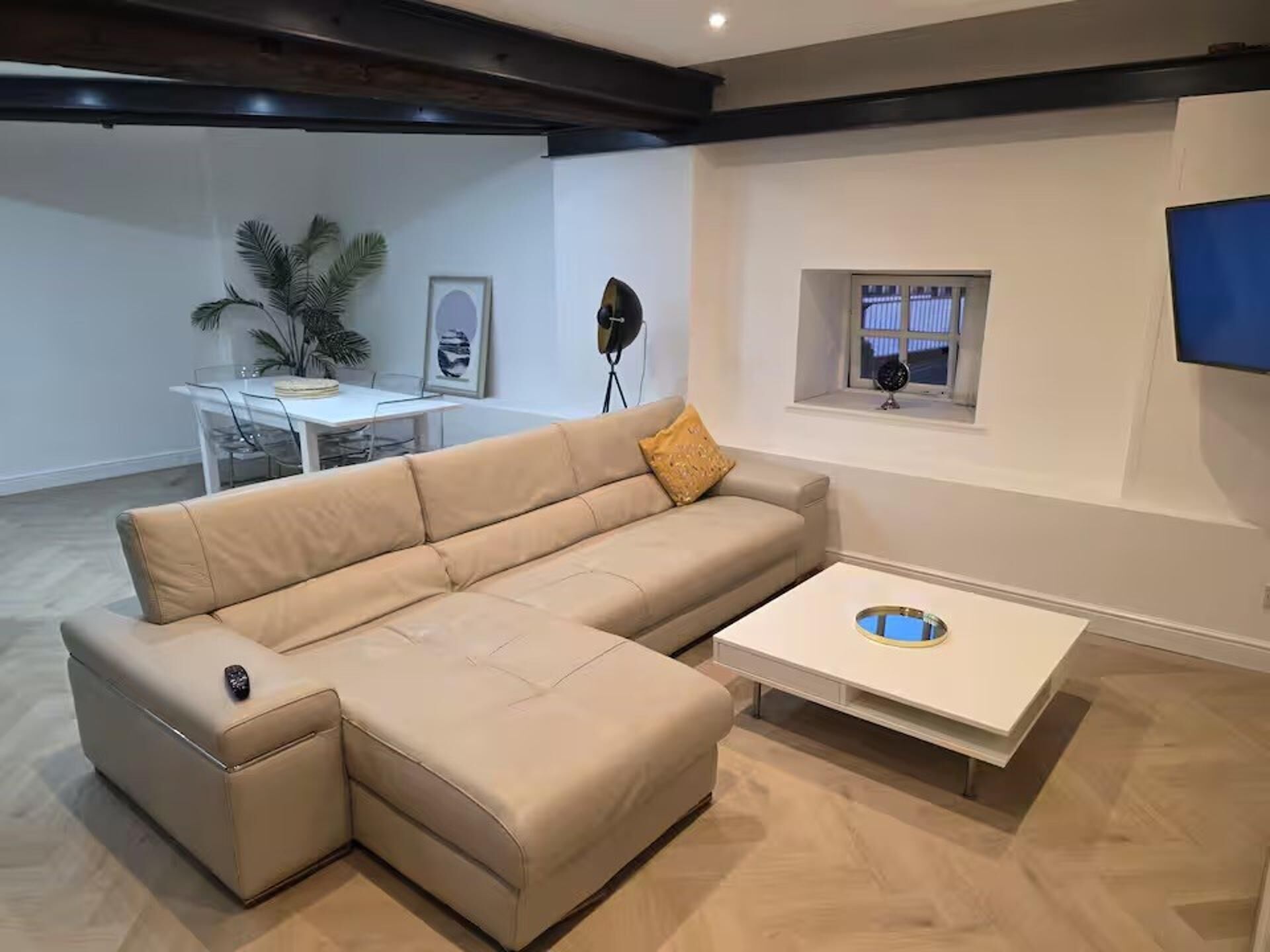 A modern living room with a sectional sofa, a coffee table, and a dining area in the background.