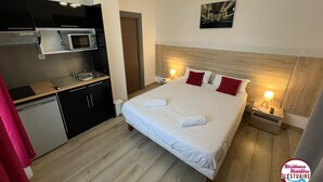 A hotel room with a bed, a nightstand, a lamp, a microwave, a sink, and a small kitchenette. - Résidence Hôtelière de l Estuaire (Le Havre)