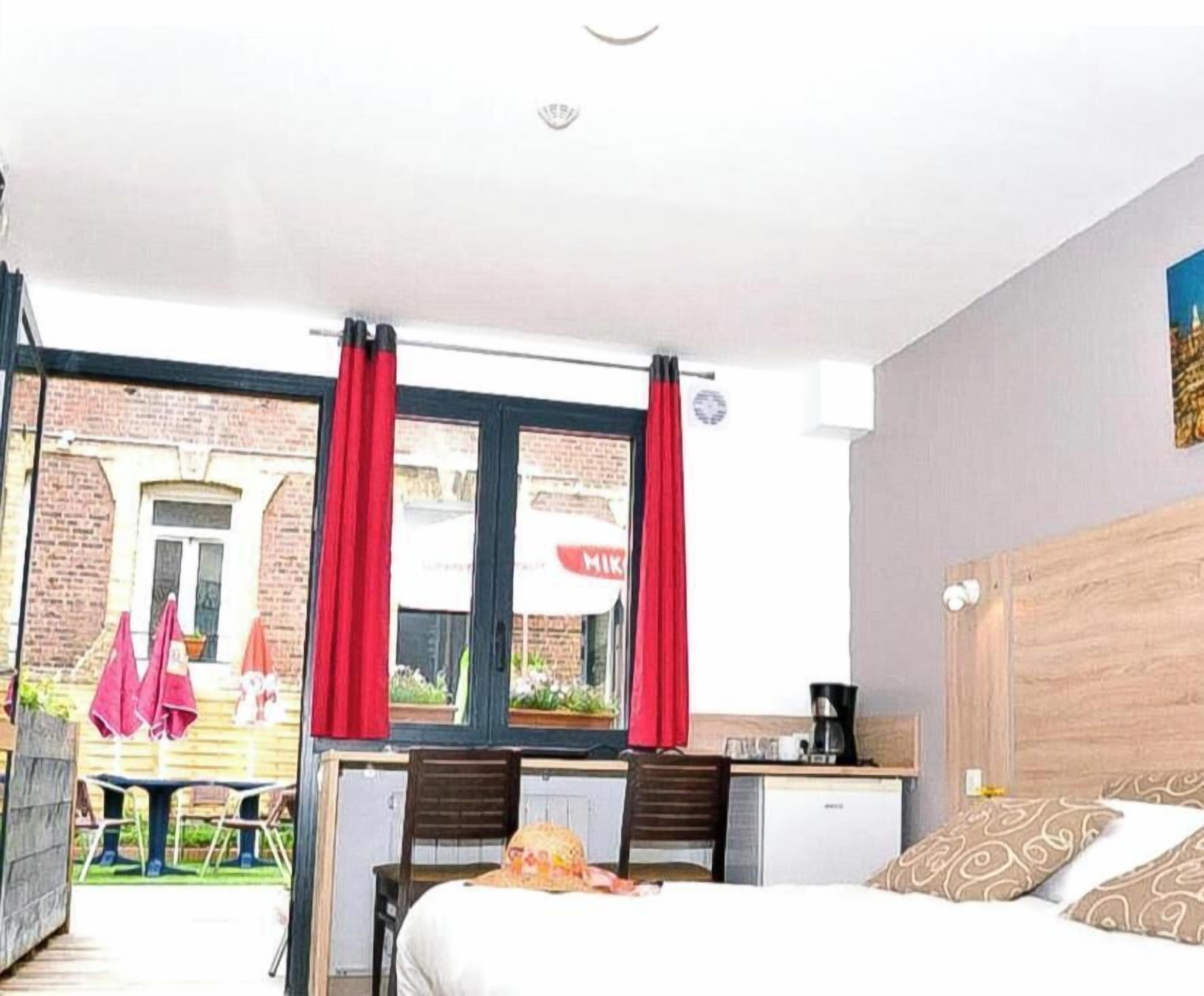 Une chambre d’hôtel avec un lit, un bureau et une fenêtre avec des rideaux rouges.