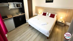 A hotel room with a bed, a small kitchenette, and a wooden floor. - Résidence Hôtelière de l Estuaire (Le Havre)