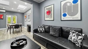 Een moderne woonkamer met een leren zwarte bank, een eettafel en kunstwerken aan de muren.