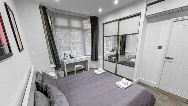 Een moderne slaapkamer met een groot bed, een bureau, een spiegel en een kledingkast.