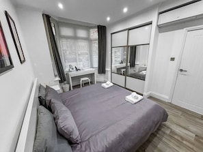 Une chambre moderne avec un grand lit, un bureau, un miroir et une armoire.