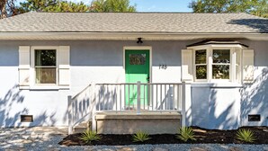 A white house with a green door, numbered 146, and a small porch with a white railing. - 4 min to beach, fully fenced yard + games, pet and kid friendly! (Oak Island)