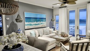 Un salon agrémenté d’un grand tableau représentant une plage, d’un ventilateur de plafond et offrant une vue sur un paysage enneigé à travers les portes vitrées.
