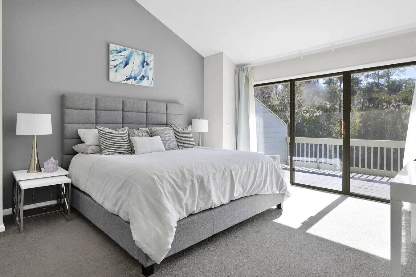 A bedroom with a large bed, a nightstand, a lamp, and a view of a balcony.
