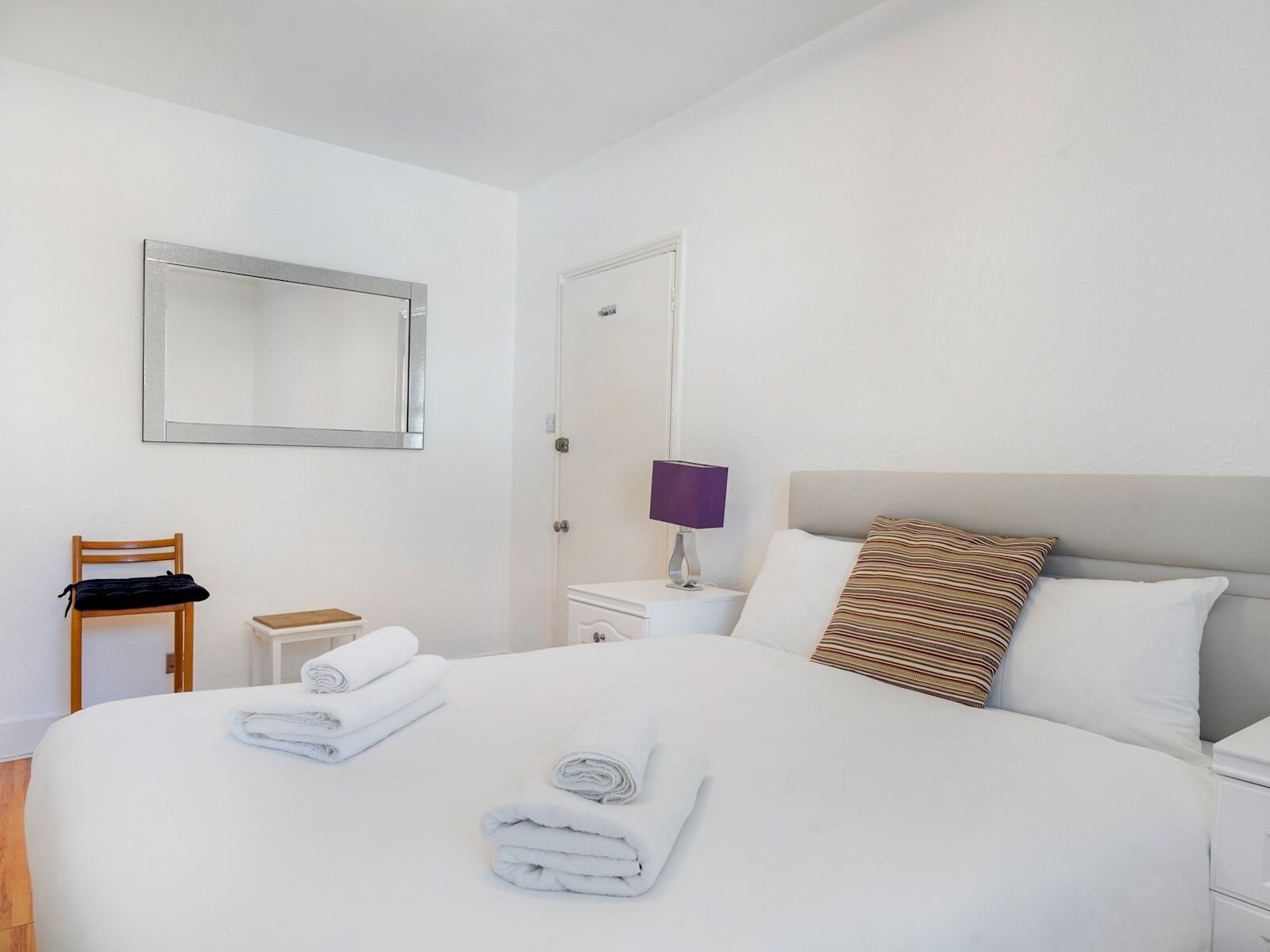 A hotel room with a large bed, a chair, a nightstand with a lamp, and a mirror on the wall.