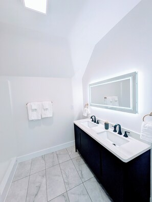 Ein modernes Badezimmer mit zwei Waschbecken, einem großen Spiegel und weißen Handtüchern an Haken.