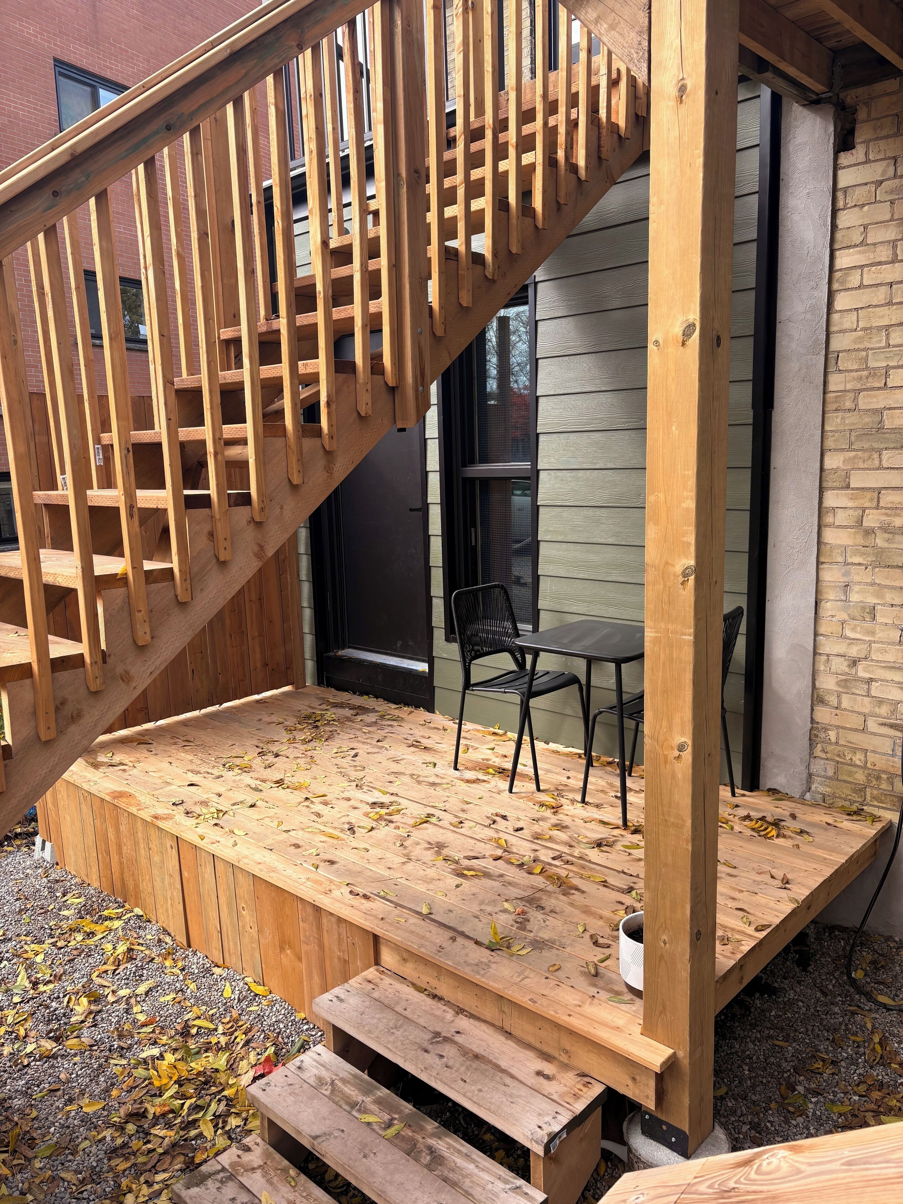A wooden deck with a staircase leading to a covered area, a table, and chairs.
