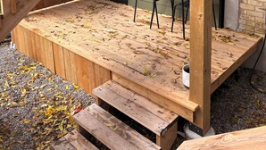 Una terraza de madera con una escalera que lleva a un espacio cubierto, una mesa y sillas.