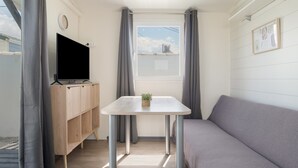 Ein Zimmer mit einer Couch, einem Tisch mit Pflanze, einem Fernseher auf einer Holzkommode und einem Fenster mit Vorhängen.