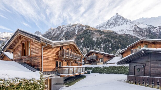 Un chalet en bois doté d’un balcon, situé au pied d’une montagne enneigée.