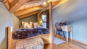 Une chambre confortable avec un plafond en bois, un lit agrémenté de serviettes roulées, un bureau avec une chaise et une fenêtre donnant sur des arbres.