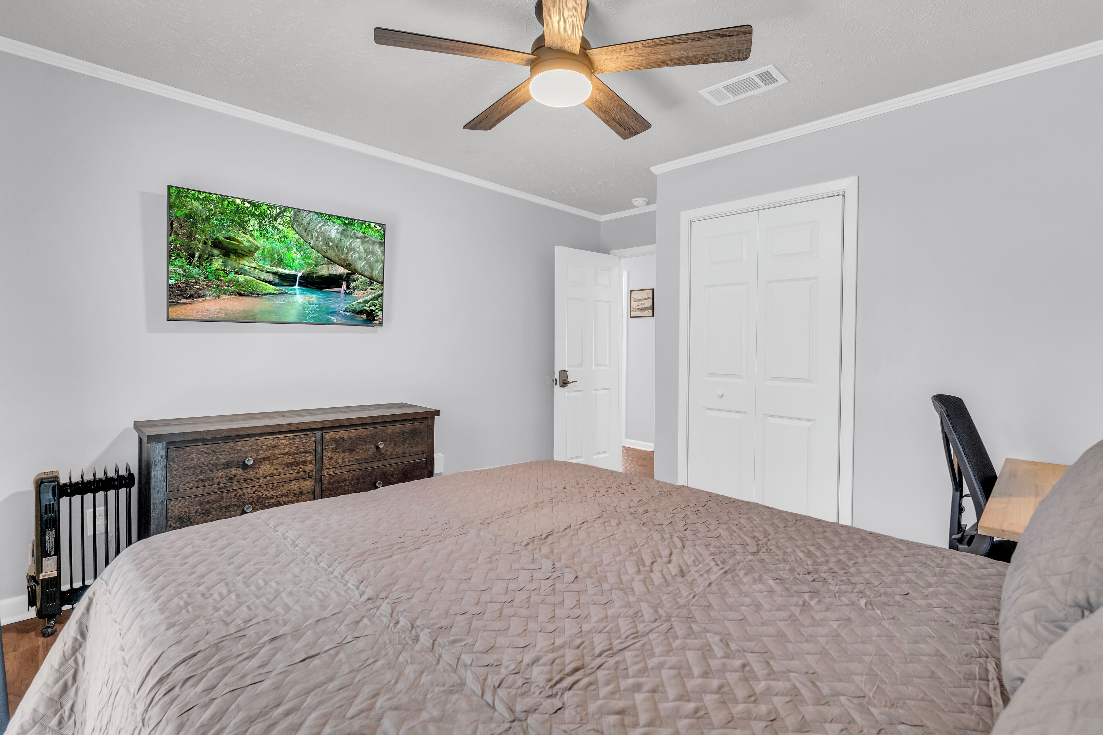 A bedroom with a bed, a ceiling fan, a dresser, a radiator, and a door.