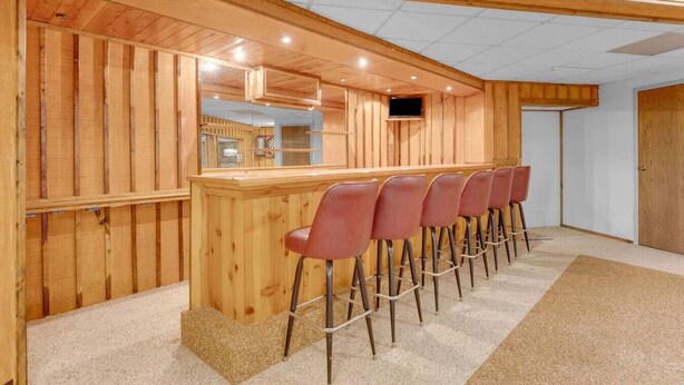 Un intérieur en bois avec un espace bar, de nombreux tabourets de bar rouges et un plafond doté d’un éclairage encastré.