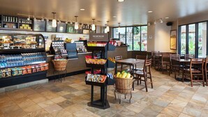 Interior de una cafetería con una vitrina de pastelería, zona de estar y mostrador con aperitivos y bebidas.