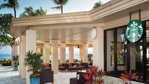 Zona de estar exterior con mobiliario de mimbre y plantas en macetas, con vistas al mar.