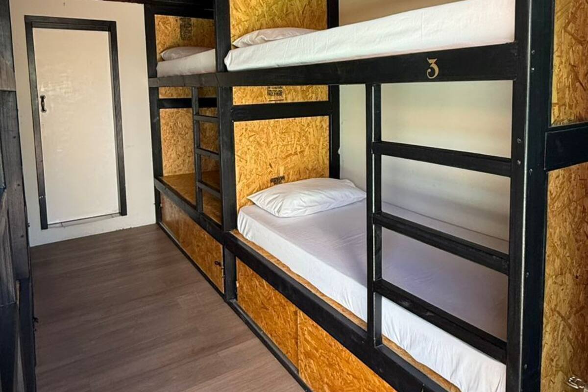 Een slaapkamer met stapelbed, plafondventilator, houten vloer en een deur.
