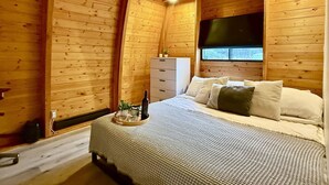 Acogedor dormitorio de cabaña de madera con una cama, un tocador y una ventana con vistas.