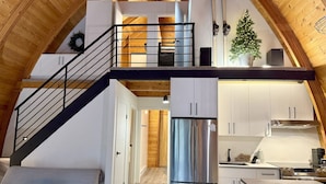 Una cocina moderna estilo loft, con una isla central, un refrigerador de acero inoxidable y una escalera de madera que sube a un nivel superior.