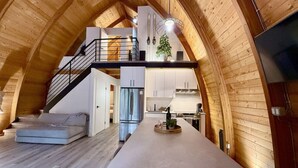 Un loft amplio con techo alto, un entrepiso y una cocina central alargada.