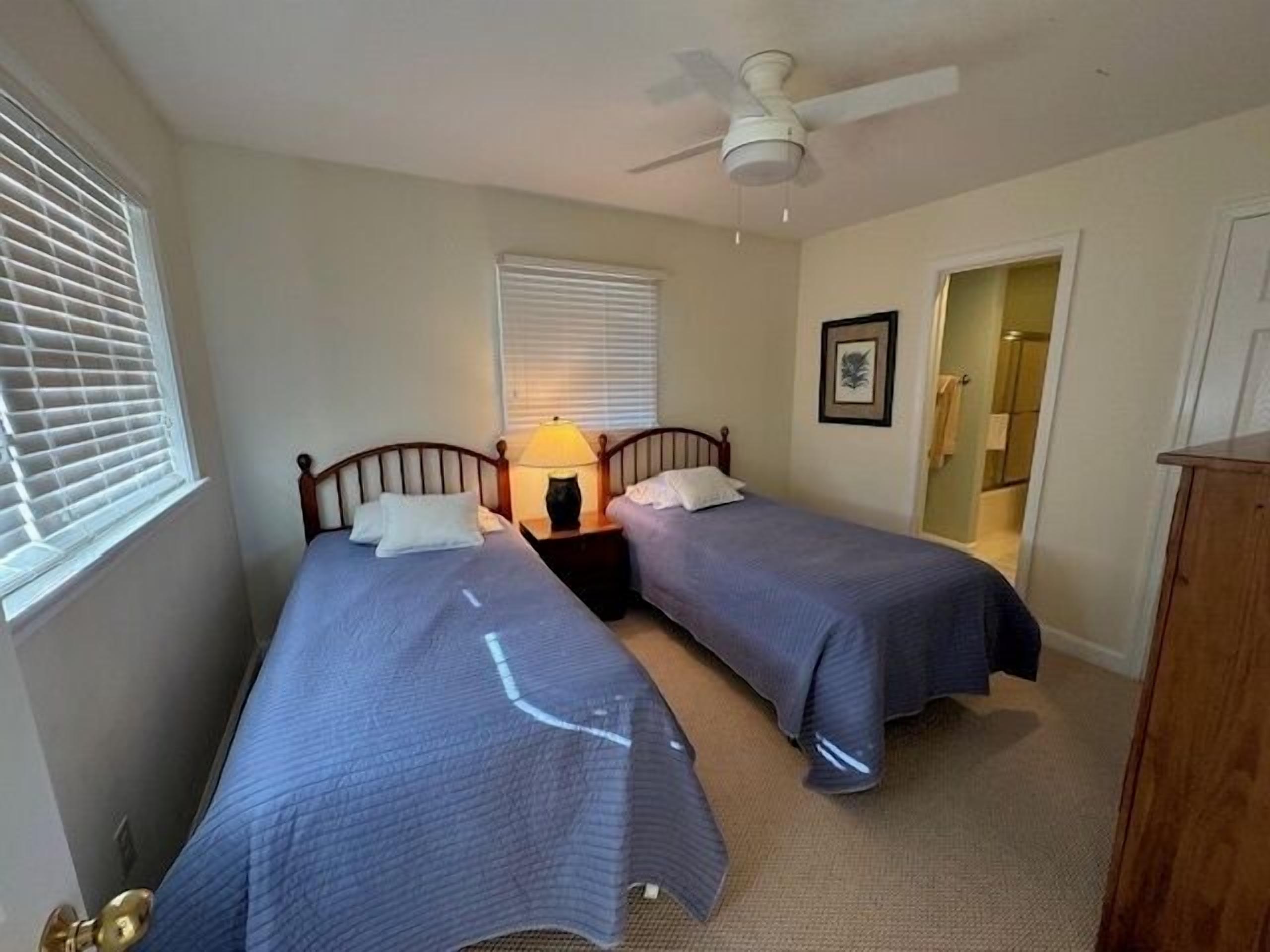A bedroom with two beds, a ceiling fan, and a nightstand with a lamp.