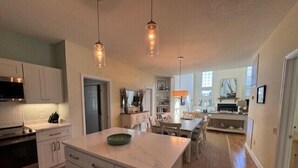 Une cuisine moderne avec des meubles blancs, un îlot en marbre et des luminaires suspendus.