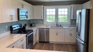 A modern kitchen with white cabinets, stainless steel appliances, and a window providing a view of greenery.