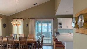 A dining area with a wooden table and chairs, a chandelier, and a view of the outside through a sliding glass door.