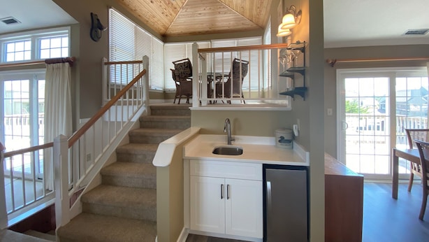 A kitchen with a wooden ceiling, a staircase, and a dining area with wicker chairs.