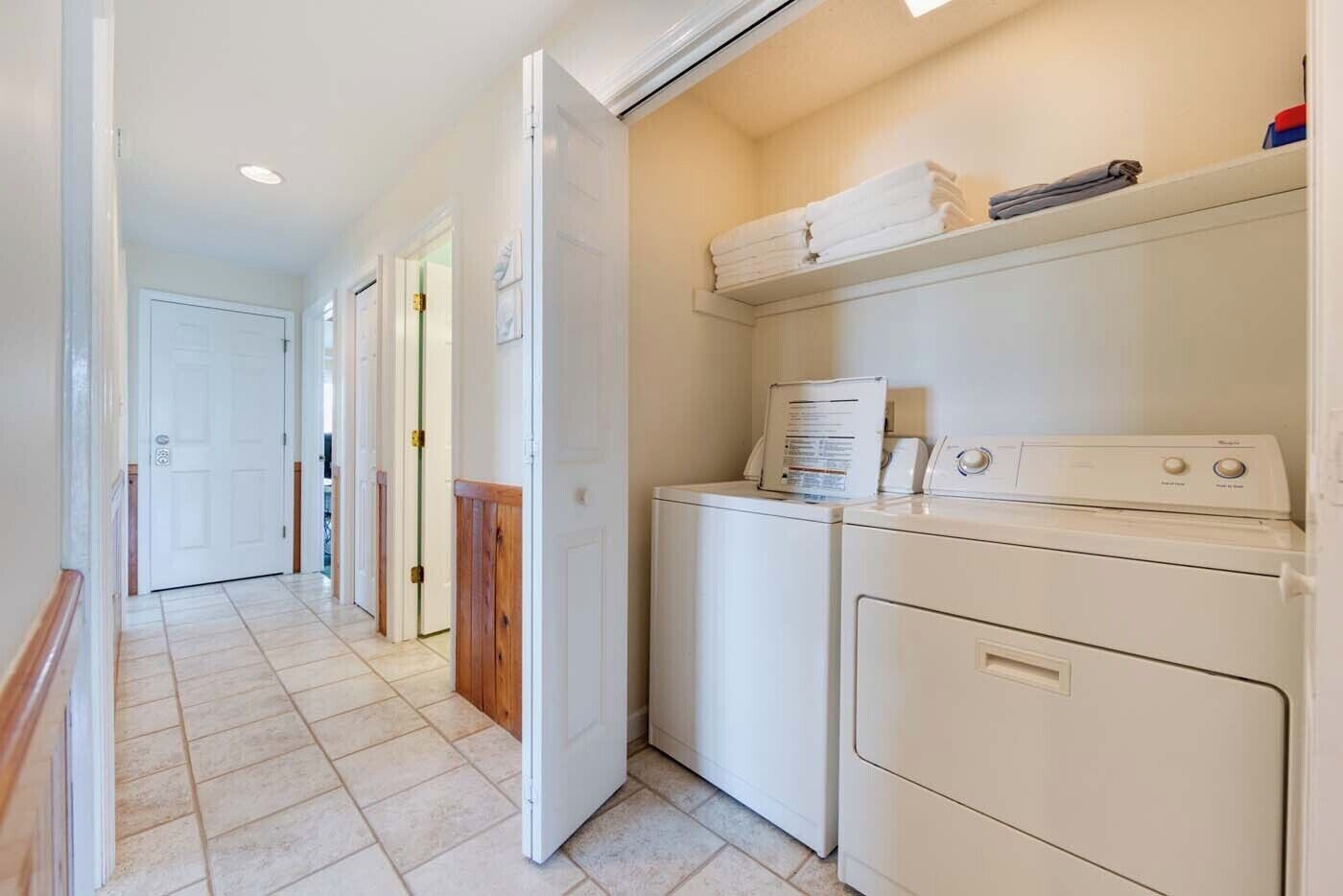 A laundry room with two washing machines, a dryer, and a shelf with folded towels.