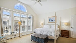 Ein Schlafzimmer mit großem Fenster, einem Bett, einem Nachttisch, einer Kommode, einem Schaukelstuhl und einer Schubladeneinheit.