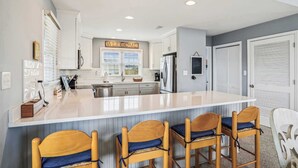 Una cocina moderna con una isla central, armarios blancos y un letrero que dice 'WELCOME' sobre la ventana.